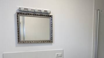 Un baño con lavamanos blanco, un espejo con marco decorativo y cabina de ducha.