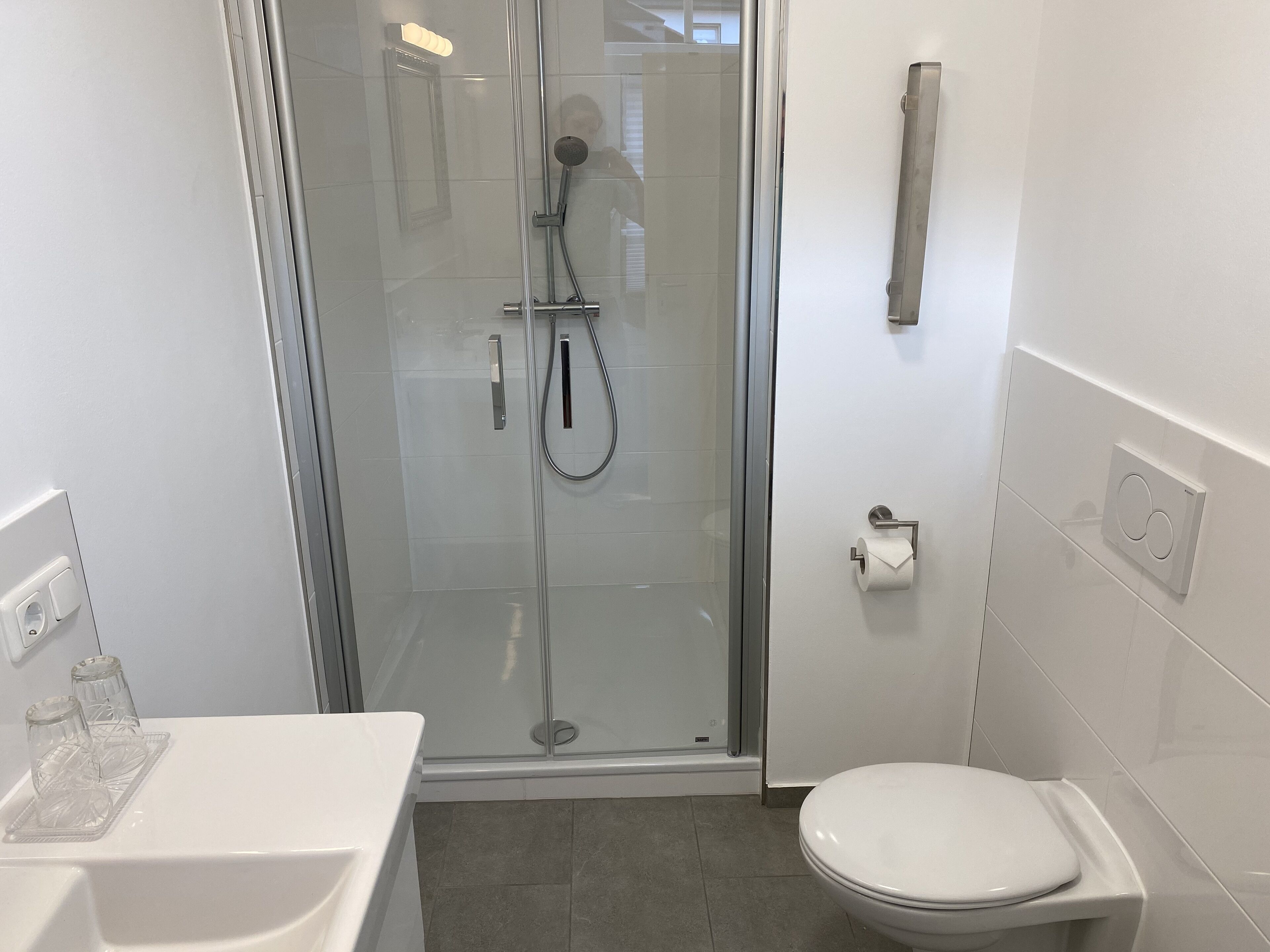 Un baño moderno con ducha acristalada, inodoro blanco y lavabo con bandeja de vidrio.