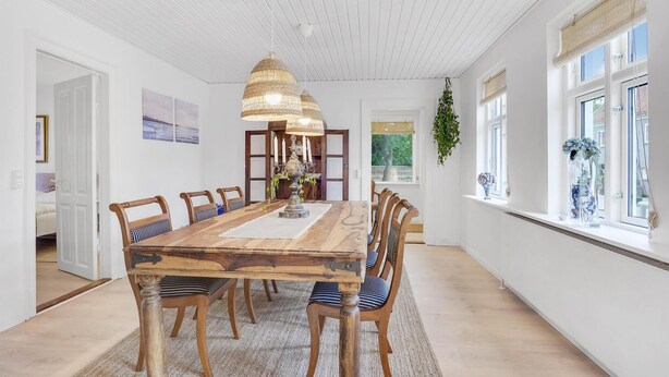 Ein Esszimmer mit Holztisch und -stühlen, einer Pendelleuchte und Blick ins Freie durch große Fenster.