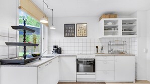 Eine moderne Küche mit weißen Schränken, einem eingebauten Backofen, einer Kaffeemaschine und einem Fenster mit Blick ins Grüne.