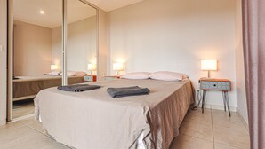 Een hotelkamer met een groot bed, twee nachtkastjes met lampen, een spiegel en een gordijn.