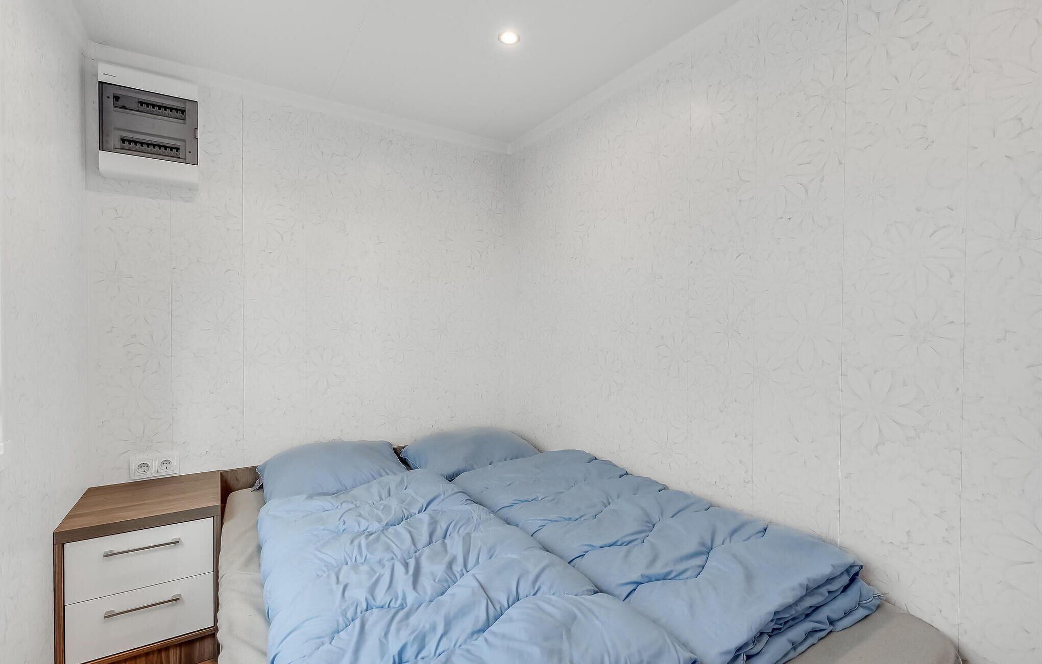 Une chambre à coucher avec un lit, une table de chevet en bois et une prise électrique fixée au mur.