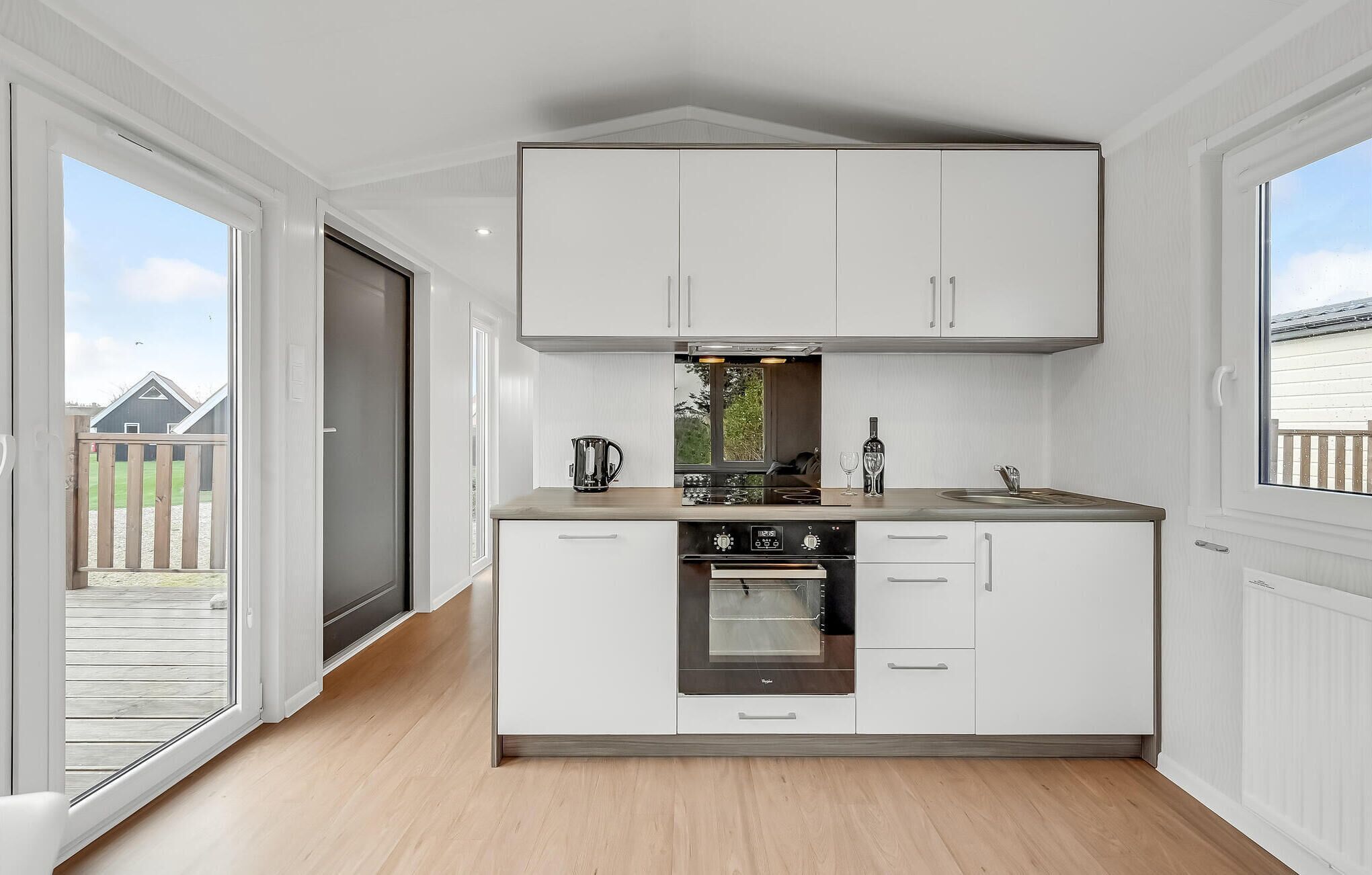 Una cucina compatta con mobili bianchi, forno integrato e finestra con vista su un patio.