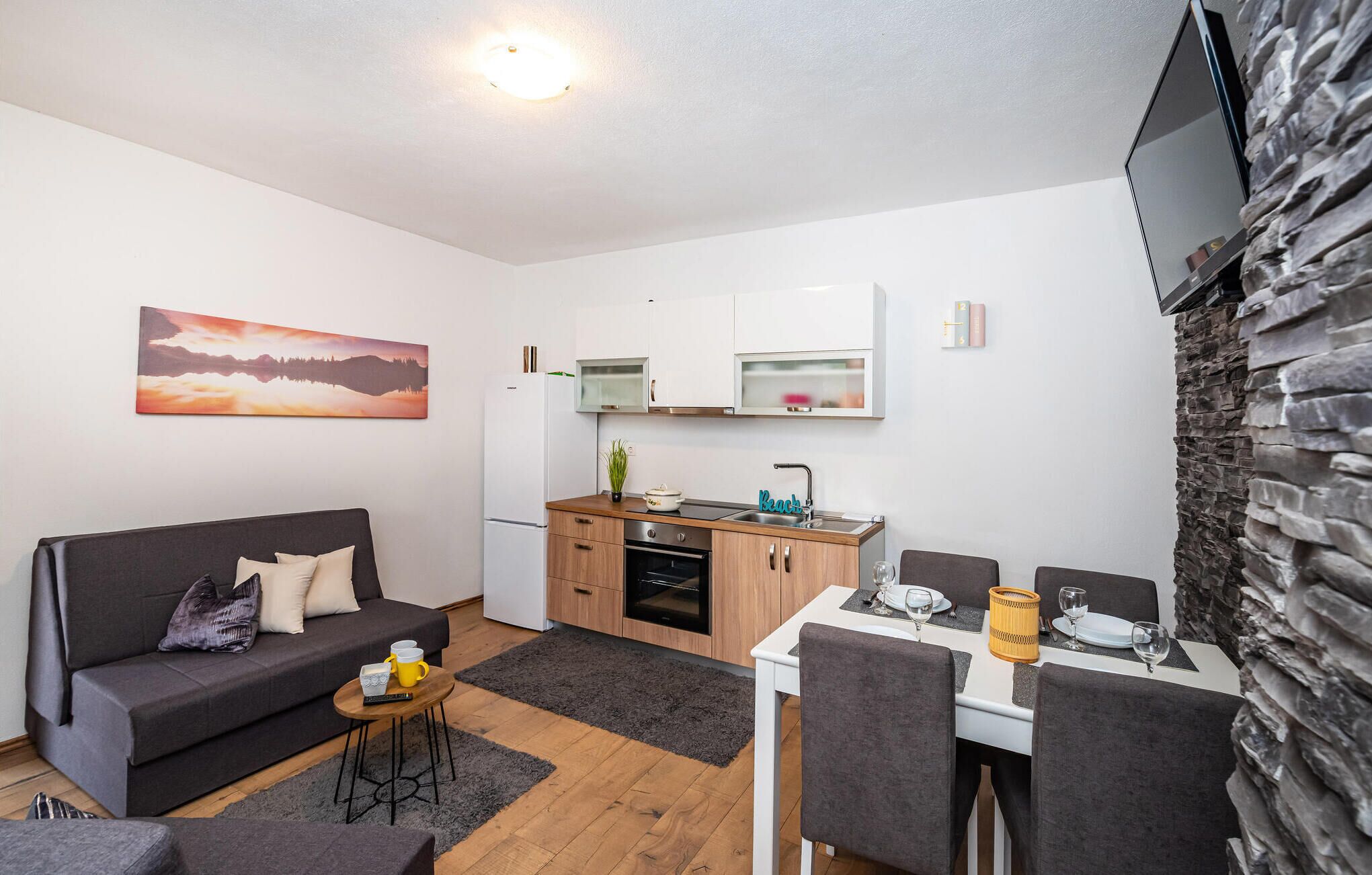 A compact living space with a sofa, a dining table set for two, a kitchenette, and a stone accent wall.
