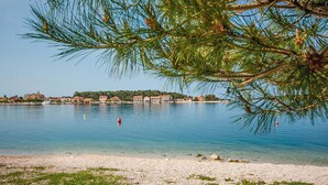 A coastal scene with a clear view of a beach, calm water, and a row of buildings in the background.