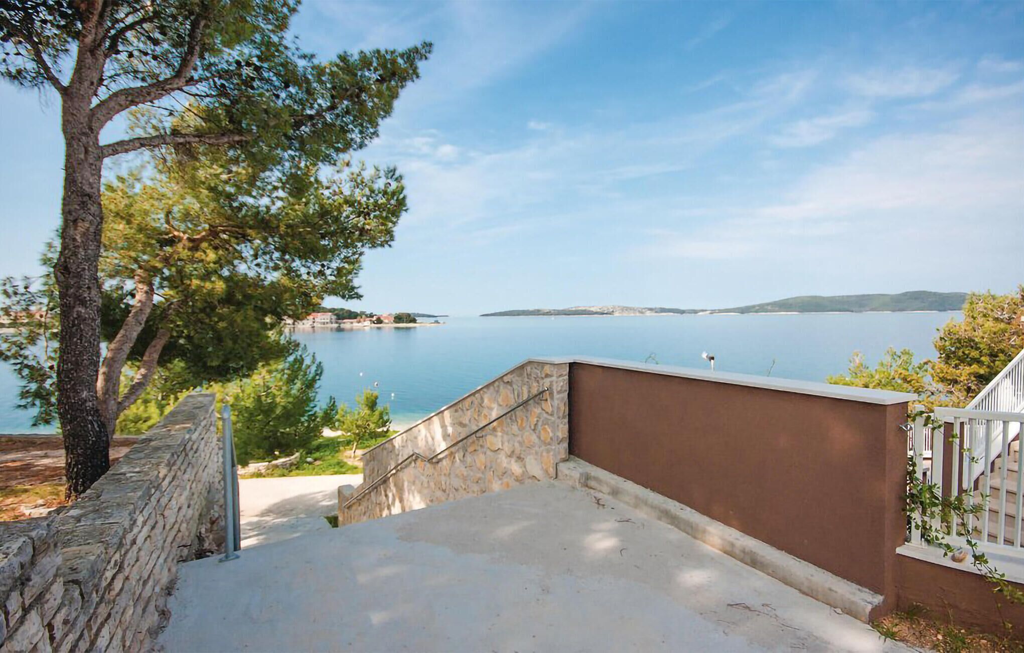 En ejendom ved kysten med en stentrappe, der fører op til en balkon med udsigt over et roligt hav og fjerntliggende landskab.