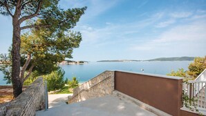 A coastal property with a stone staircase leading to a balcony overlooking a calm sea and distant land.