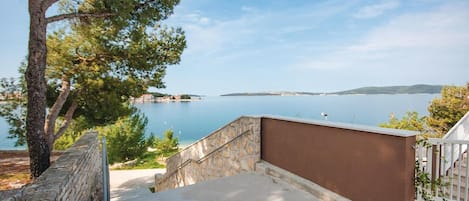 En ejendom ved kysten med en stentrappe, der fører op til en balkon med udsigt over et roligt hav og fjerntliggende landskab.