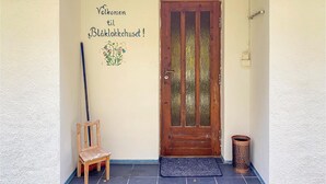 Una puerta de madera con un panel de vidrio, una silla de madera, un cartel de bienvenida y un cubo de basura frente a un edificio.