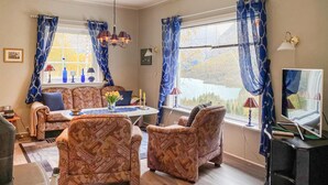 Una sala acogedora con mobiliario estampado, una mesa de comedor y vistas a un lago a través de amplias ventanas.