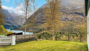 Vista de un paisaje montañoso con un lago, una valla de madera y una zona cubierta de césped.