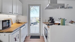A modern kitchen with white cabinetry, a wooden countertop, and a view through a glass door to an outdoor patio. - Cozy home in Hadsund with WiFi (Hadsund)