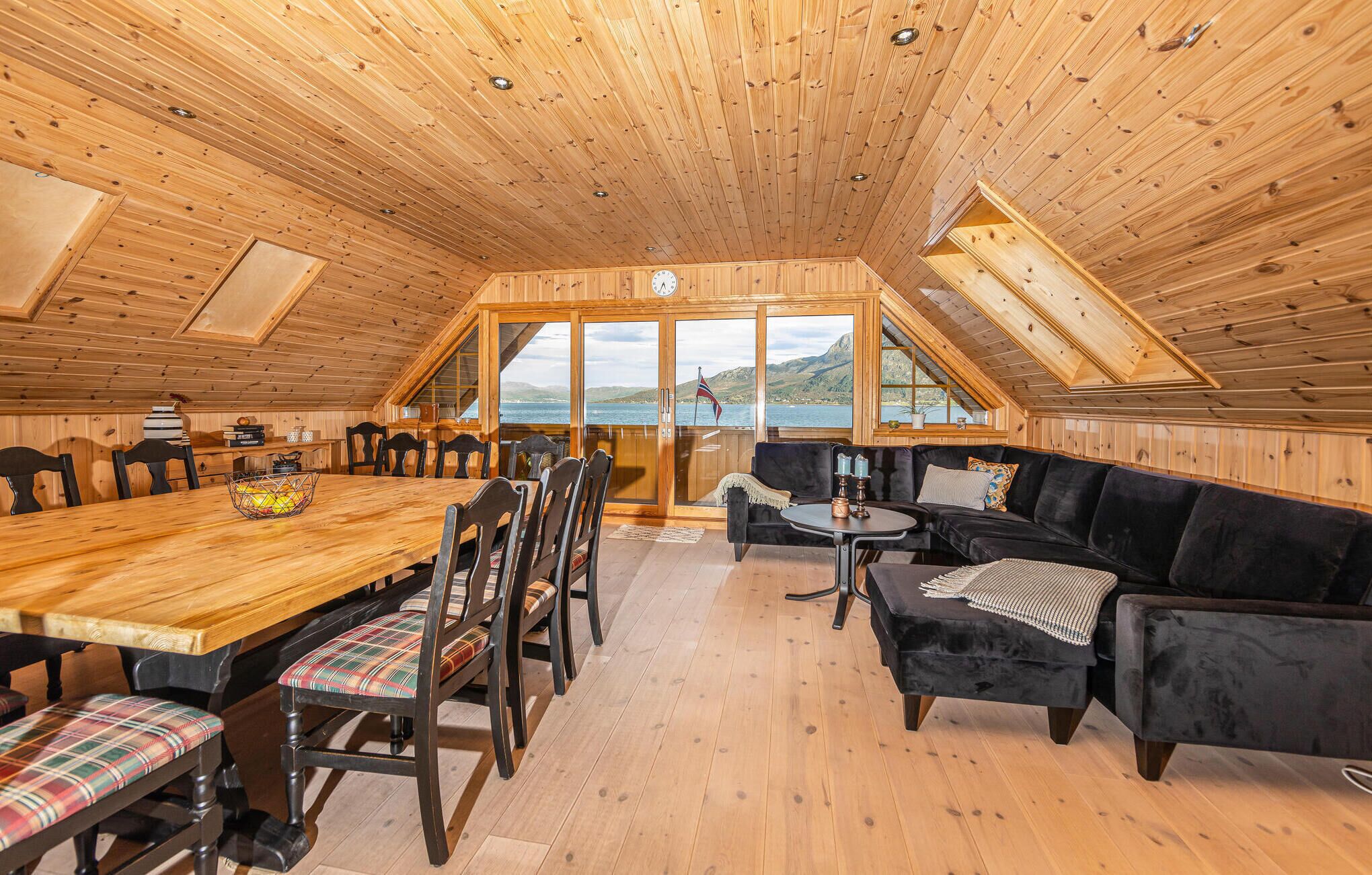 A wooden cabin with a dining area, a sofa, and a view of the lake.