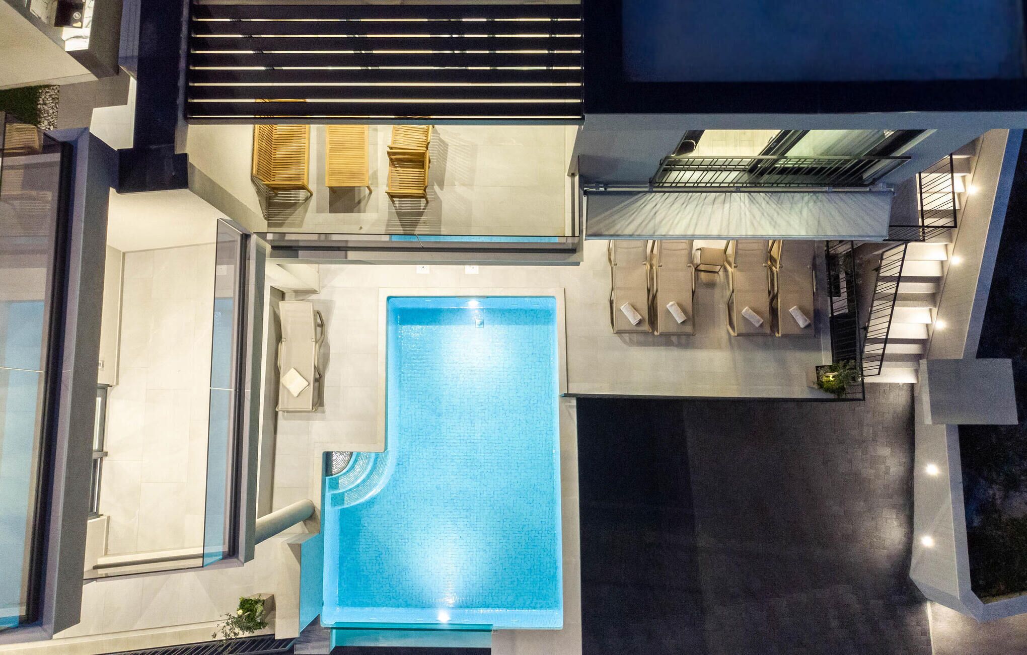 Un espace piscine aménagé sur le toit, avec une piscine rectangulaire, des chaises longues et un escalier menant à une terrasse supérieure.