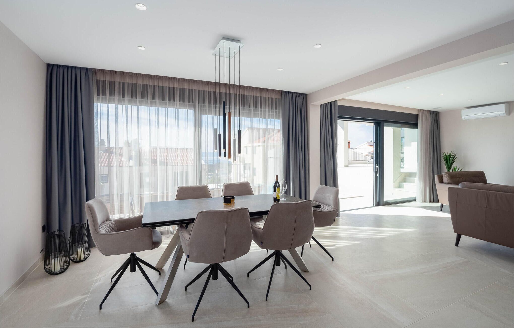 A modern dining area with a round table, six chairs, and a bottle of wine.