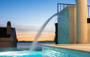 Una piscina con fuente, pared de azulejos y vista al agua al atardecer.