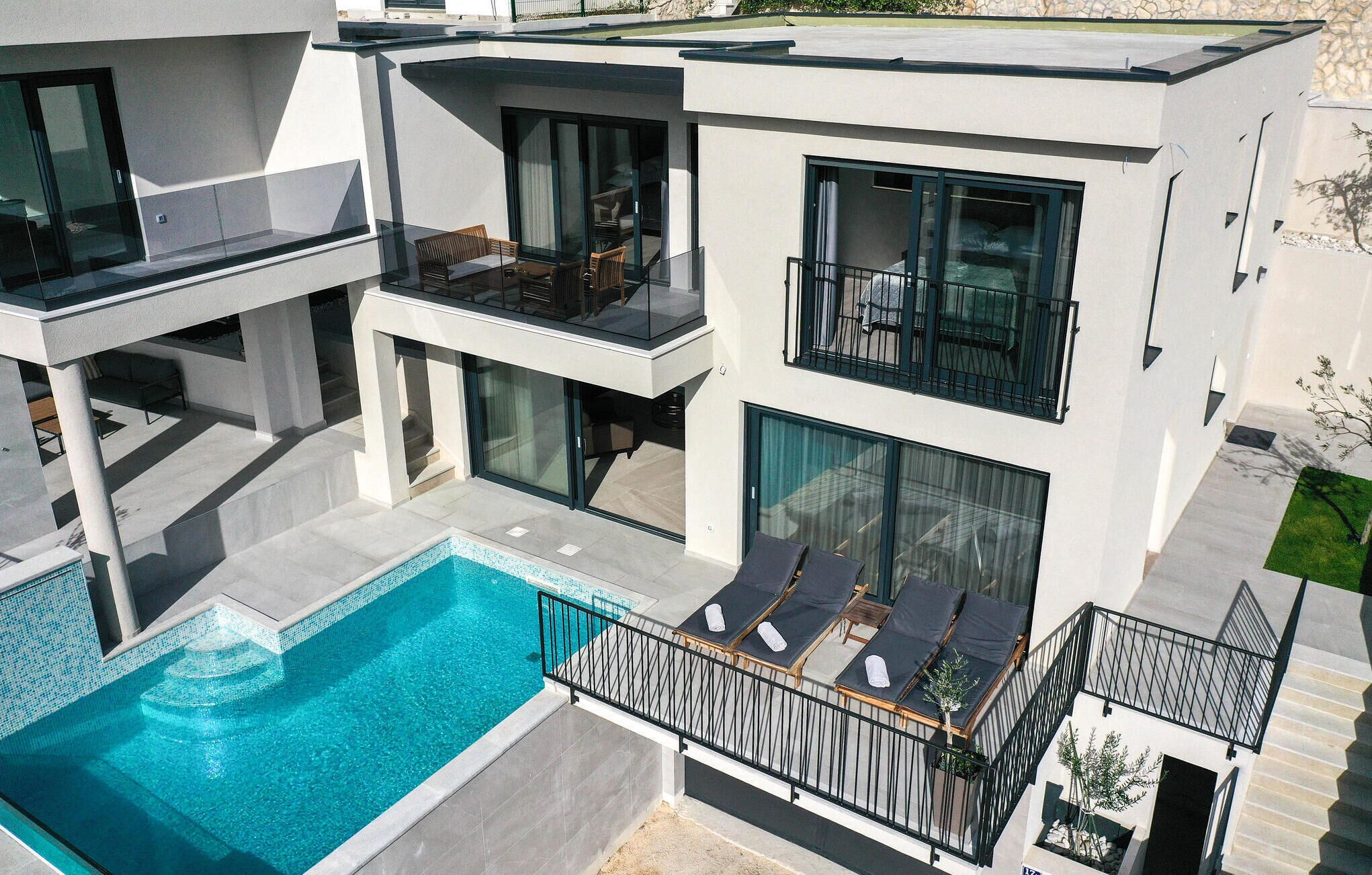 A modern multi-story house with a swimming pool, balconies, and outdoor seating areas.