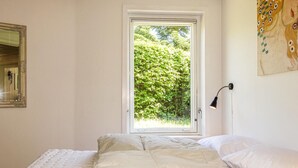 A bedroom with a bed, a window with a view of greenery, a wall-mounted lamp, and a mirror. - 3 bedroom lovely home in Rønne (Rønne)