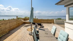Eine Holzterrasse mit Meerblick, eine überdachte Sitzgruppe und ein Tisch mit Stühlen.