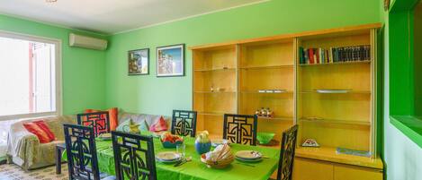 A dining area with a green table, chairs, and a bookshelf.