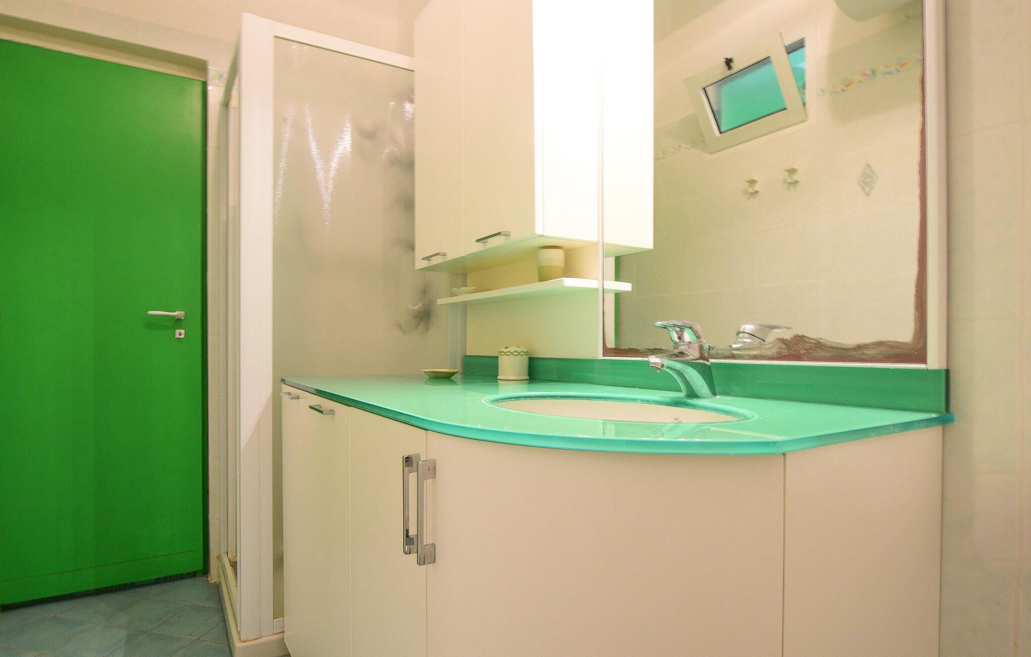 Ein Badezimmer mit grüner Tür, einem Waschbecken mit Spiegel darüber und einer Toilette im Hintergrund.