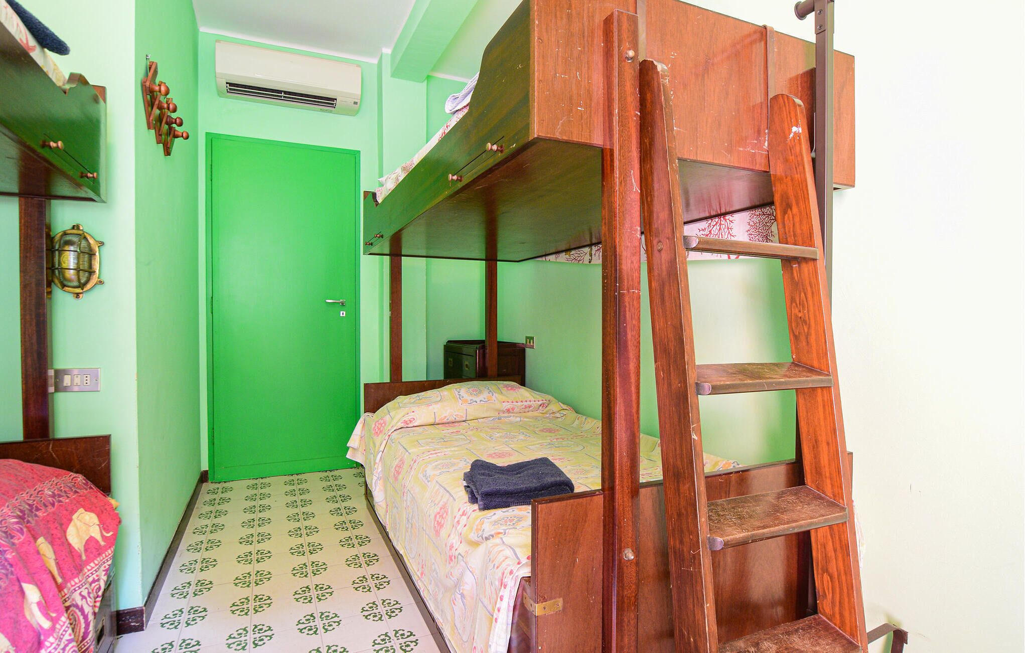 A small, compact room with a bunk bed, a wooden ladder, a small table, and a green door.