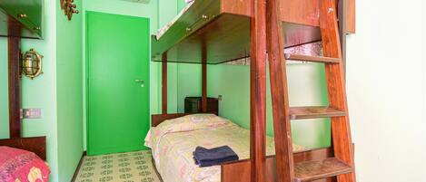 A small, compact room with a bunk bed, a wooden ladder, a small table, and a green door.