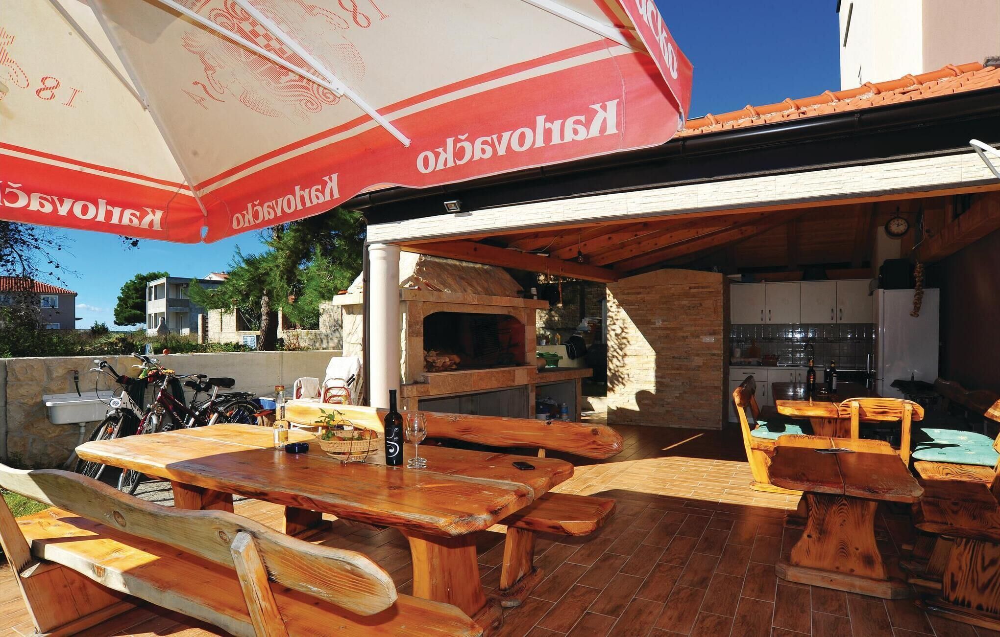 An outdoor dining area with wooden tables and benches, a pizza oven, and a large umbrella.