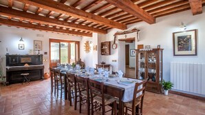 A dining area with a long wooden table set for six, surrounded by chairs. A wooden cabinet with glass doors is to the right, and a rustic wooden ceiling with exposed beams is above. - Lovely home in Tolentino with kitchen (Tolentino)