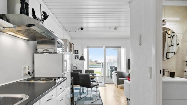 Een moderne keuken met witte kasten, een zwart aanrecht en een zichtbare kookplaat. Er is een eethoek met een tafel en stoelen, en uitzicht op de omgeving door een glazen deur.
