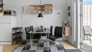 Een moderne keuken met een eethoek, met een centraal kookeiland, zwarte stoelen en een zwarte hanglamp.