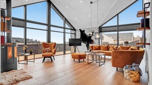A spacious living room with large windows, a fireplace, a sofa, and a bear mounted on the wall.