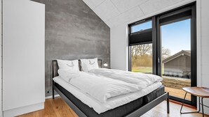 A modern bedroom with a bed, a nightstand, and a view of the outdoors.