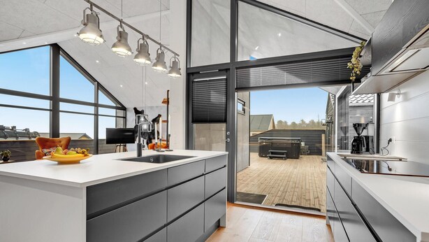 A modern kitchen with a large island, a view of the outdoor deck, and a dining area with a table and chairs.
