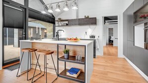 A modern kitchen with a central island, bar stools, a sink, and a fruit bowl.