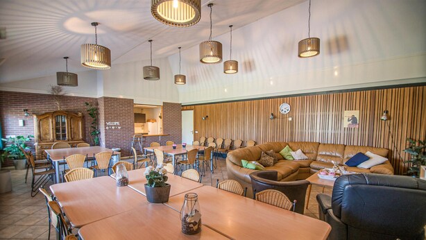 Een ruime binnenruimte met meerdere houten tafels en stoelen, een leren bank en hangende吊り灯.