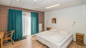 Een hotelkamer met een tweepersoonsbed, een houten stoel, een kleine tafel en een radiator.