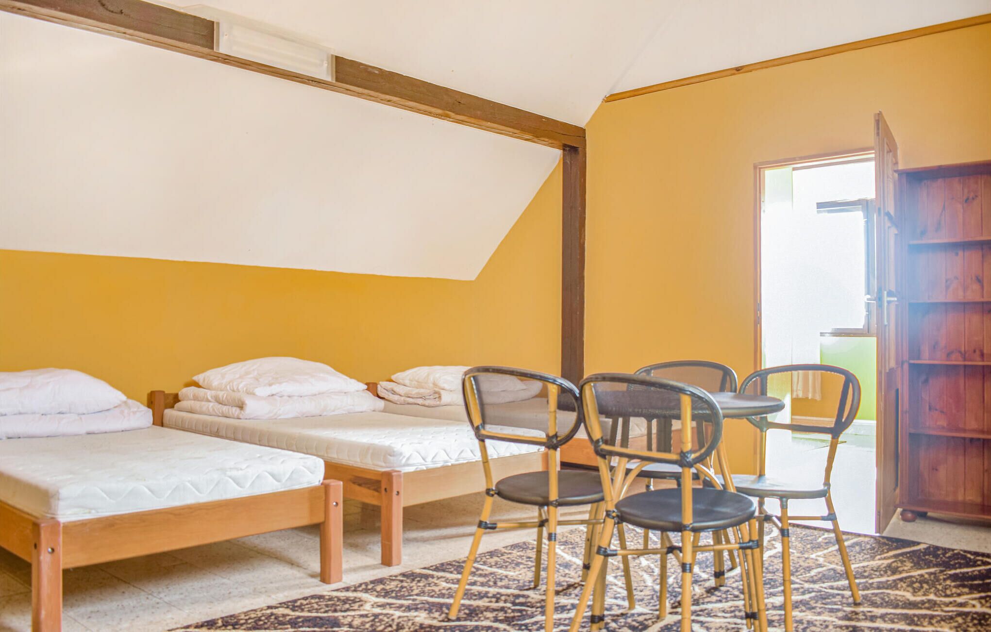 A room with two single beds, a small table with chairs, and a wooden cabinet.