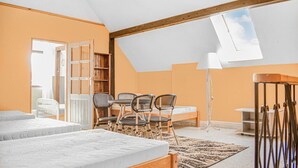 Un dormitorio con techo inclinado, tragaluces, cama, escritorio, sillas, lámpara y estantería.