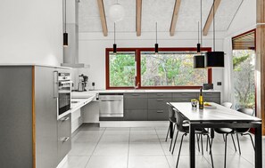 A modern kitchen with stainless steel appliances, a dining area with a table and chairs, and large windows offering a view of trees. - Lovely home in Grenaa with WiFi (Grenaa)