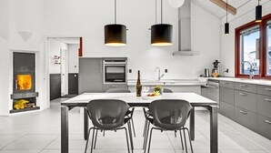 Ett modernt kök med en central köksö, två hänglampor och utsikt över utemiljön genom ett fönster.