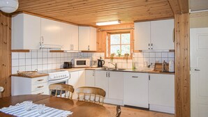 Une cuisine compacte avec des meubles blancs, un plafond en bois, une fenêtre ornée de plantes, une cuisinière, un four à micro-ondes et un évier.