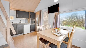 Una cucina moderna con mobili grigi, un frigorifero bianco e un forno. C'è un tavolo da pranzo con sedie e una finestra con vista sugli alberi.
