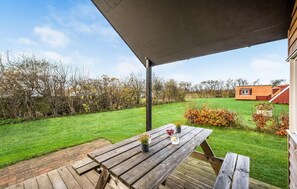 A wooden deck with a picnic table, a covered area, and a view of a house with a red roof and a small garden.