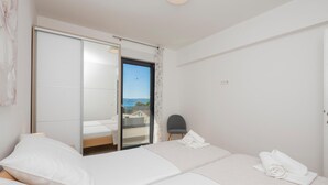 Une chambre d’hôtel avec un lit, une chaise, une vue sur la mer et une porte coulissante donnant sur le balcon.