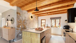 A modern kitchen with wooden beams, a central island with a fruit platter, and a stone wall with a leaf mural. - Gorgeous home in Blato (Blato)
