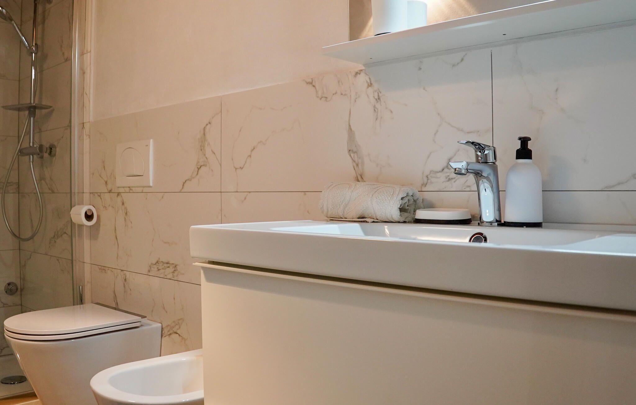 A modern bathroom with a marble backsplash, a white sink, a handheld showerhead, and a toilet.