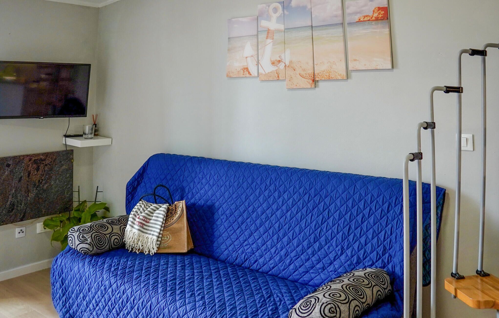 A blue quilted sofa with patterned pillows, a mounted TV, and a wall with three framed pictures.