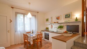 A compact kitchen with a dining area, wooden flooring, and a TV on the counter.