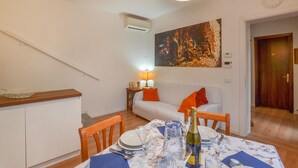 A dining area with a table set for two, a white sofa, a painting on the wall, and an air conditioning unit.